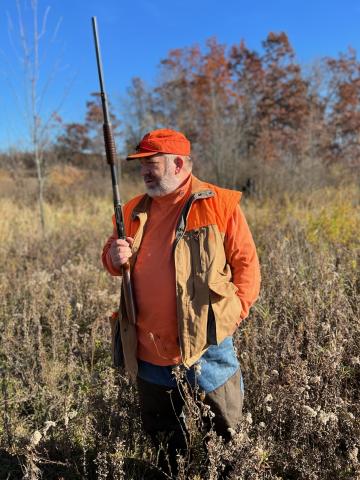 man in orange shirt and hat, holding hunting rifle