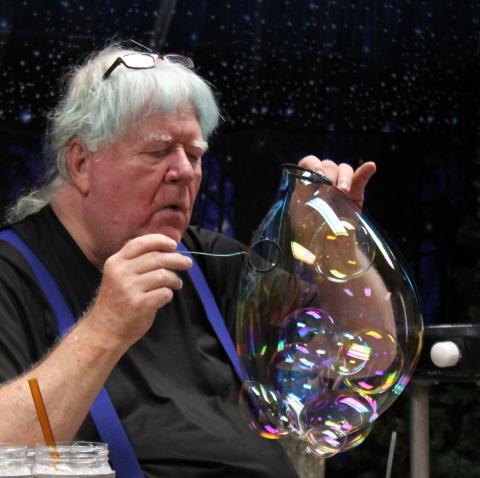 Man in black shirt with white hair, blowing bubbles